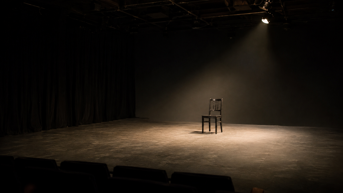 Empty black box theater stage with a single chair illuminated by a soft spotlight, representing space for reflection and possibility.